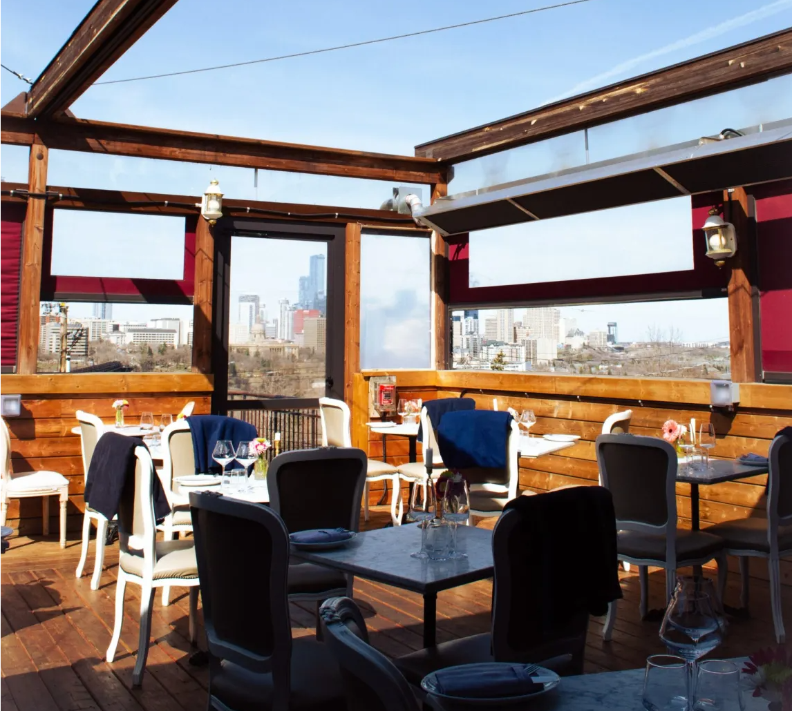 Covered rooftop patio with wood-beam pergola and table seating overlooking the downtown Edmonton skyline